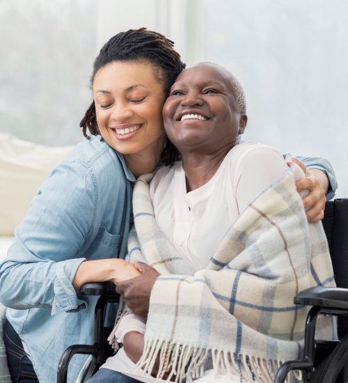 Loving young woman gives her elderly mother a hug. The older woman is in a wheelchair and is wrapped in a warm blanket.